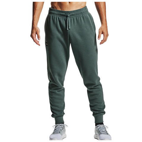 Green sweatpants are worn by a person standing with their back facing the viewer while wearing grey athletic shoes in a neutral light setting. There is a pocket at the back.