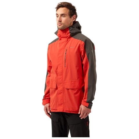 A man is standing confidently wearing a bright red waterproof jacket with gray accents and multiple pockets set against a plain white background