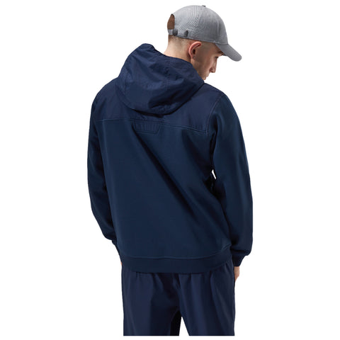 A person wearing a navy blue hoodie with a hood is standing with their back to the viewer while wearing a light gray cap in a neutral setting.