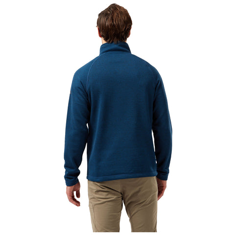 A man is wearing a blue fleece pullover with a high collar facing away from the viewer in a neutral background suggesting an outdoor or casual setting.