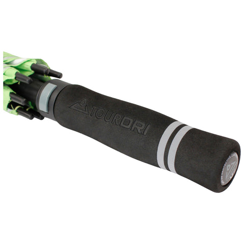 A black umbrella handle with a textured grip is positioned diagonally the top has a green canopy with black components suggesting readiness for use in rainy weather