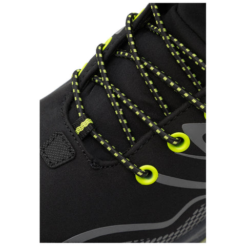 A black athletic shoe features bright green laces threaded through eyelets and a textured panel. The shoe is positioned against a neutral background, highlighting its design and details.