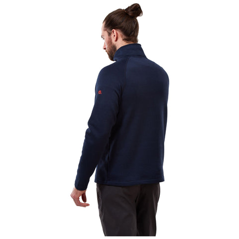 A man wearing a navy blue fleece pullover stands with his back turned slightly to the viewer in a plain white background. His hair is tied in a bun and he appears relaxed.