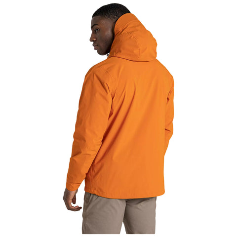 A person wearing an orange hooded jacket stands with their back turned, looking slightly over their shoulder in a minimalist setting with a plain white background.