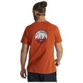 A man wearing an orange t-shirt with a mountain graphic walks away from the viewer The shirt has the words ADVENTURE GOOD FOR THE SOUL printed on the back