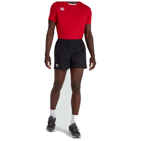 A person stands wearing a red athletic shirt and black shorts. They are in a neutral background, suggesting a focus on sportswear. The individual has on black sneakers with white socks.