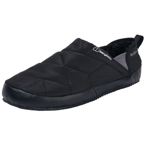 A black slip-on shoe with a quilted exterior and a textured rubber sole rests on a white surface showing a design intended for comfort and warmth indoors.