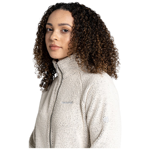 A young woman with curly hair gazes confidently at the camera while wearing a textured, light-colored jacket with a high collar against a plain white background.