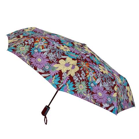 A floral-patterned umbrella is open displaying vibrant colors and various flower designs against a dark background while being held by its handle creating a whimsical appearance suitable for outdoor use.