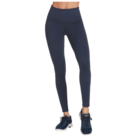 High-waisted navy leggings are being worn by a person who is standing upright. The surroundings are neutral, focusing attention on the athletic apparel and matching dark sneakers.