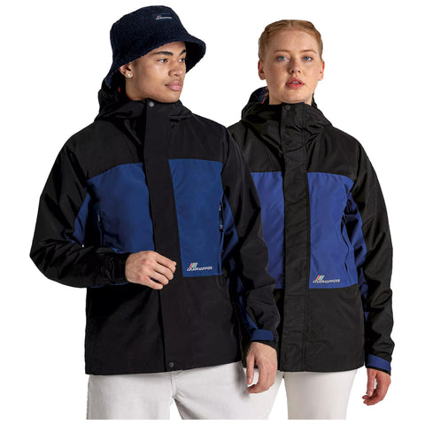 Two individuals wearing matching black and blue jackets stand side by side. The person on the left has a bucket hat, while the one on the right has their hair styled in a braid.