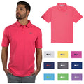 A man in a pink polo shirt stands confidently with his hands in pockets while looking thoughtfully upwards next to a display of various colored polo shirts with logos.