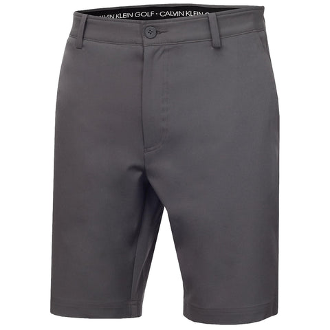 Gray golf shorts are displayed hanging vertically with a button and zipper front closure showcasing a minimalist design and a logo band around the waistband indicating Calvin Klein Golf branding.