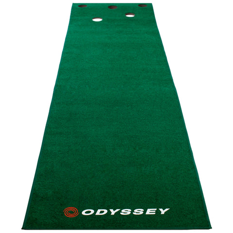 A green putting mat features circular holes at one end designed for practicing golf putting skills in a home or indoor setting with the brand name Odyssey displayed prominently.