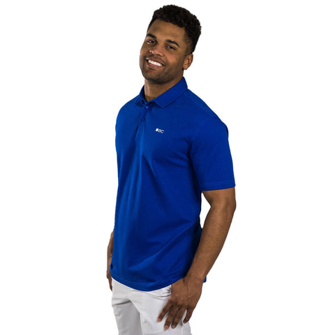 A man is smiling and standing with a slight tilt wearing a bright blue polo shirt and white pants in a plain background.