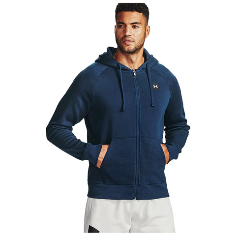 A man stands confidently wearing a navy blue zip-up hoodie with a hood and front pockets showcasing a brand logo on his chest in a neutral background.