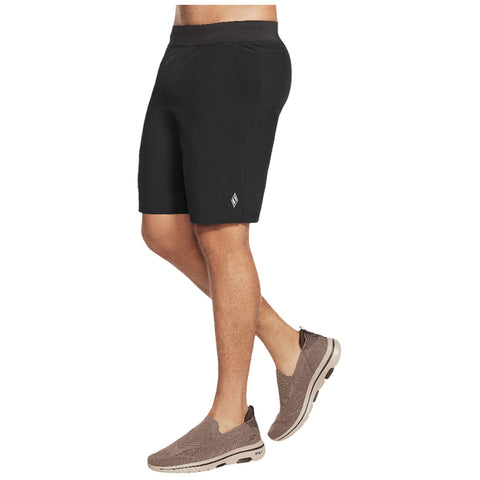 A person wears black shorts and brown slip-on shoes while standing in a neutral setting that emphasizes their casual outfit suitable for warm weather activities.