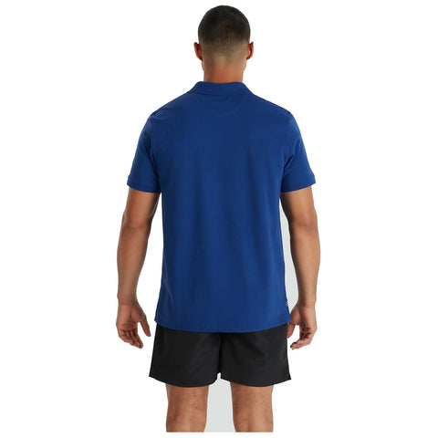 A person is standing with their back facing the viewer wearing a blue polo shirt and black shorts in a simple, unobtrusive setting that emphasizes their attire.