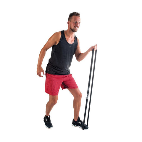 A man wearing a black tank top and red shorts is exercising with a long black resistance band while standing on one leg in a bright, minimalistic environment.