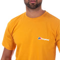 A person is wearing a vibrant yellow t-shirt featuring a small logo on the chest which reads "berghaus" with a colored design showcasing outdoor apparel in a neutral setting.