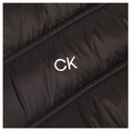 A black puffy jacket is displayed with a white embroidered CK logo prominently visible on the fabric's surface which features diagonal stitching patterns throughout.