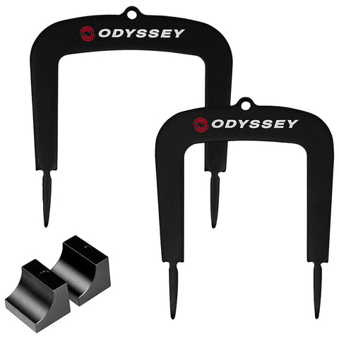 A pair of black golf divot repair tools labeled Odyssey stands upright with pointed ends used for fixing grass on golf courses beside two small black rubber pieces for securing items.