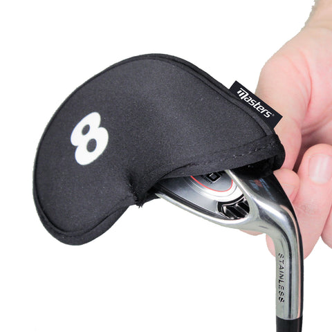 A hand holds a golf club covered with a black protective headcover marked with the number eight showcasing the shiny silver club head underneath in an indoor setting