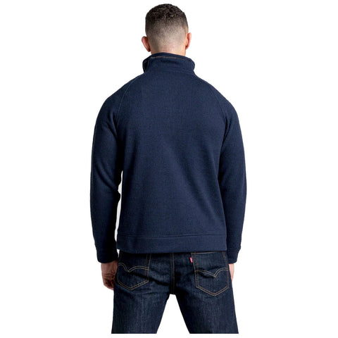 A person wearing a dark navy sweater faces away while standing. The context includes dark jeans with visible branding on the back pocket, suggesting a casual setting.