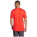 A person wearing a bright red t-shirt stands with their back to the viewer in a neutral background, suggesting a casual or relaxed environment.