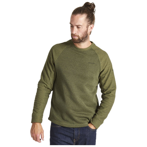 A man wearing a green sweatshirt stands with a thoughtful expression His left hand is slightly raised while his right hand rests in his pocket against a plain white background