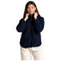 A woman wears a dark navy, fluffy zip-up jacket while adjusting her collar with both hands in a neutral background, suggesting a casual or outdoor setting.