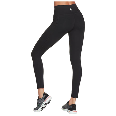 Black leggings are worn on a person’s lower body while standing in a casual pose alongside a sneaker on the foot creating a sporty appearance in a neutral background.