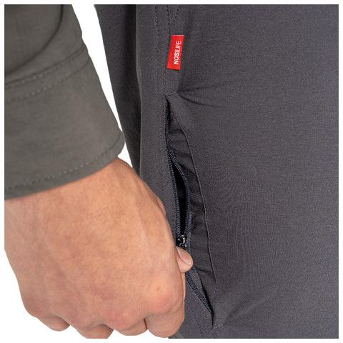 A hand is grasping a zipper on the side of a pair of dark gray pants revealing an inner pocket detail in a neutral setting with a focus on practical apparel design.