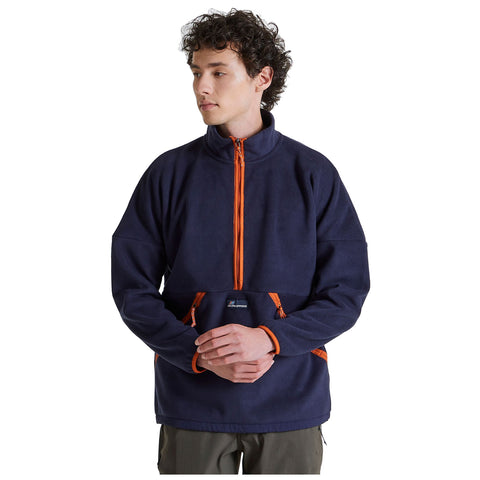 A young man wears a navy fleece jacket with orange zippers and details while standing calmly with his arms crossed in a plain white background.