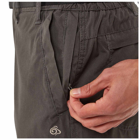 A hand is pulling down the zipper of a side pocket on dark gray pants showcasing the texture and seam details in a casual indoor setting