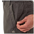 A hand is unzipping a pocket on a pair of gray pants located in a neutral setting highlighting the fabric texture and stitching details around the pocket area.