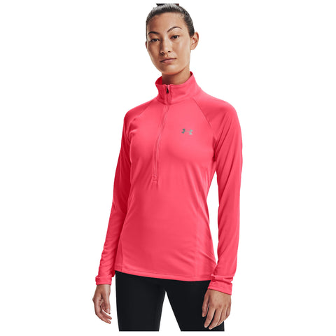 A woman stands confidently wearing a bright pink long-sleeve athletic shirt with a quarter zipper and the Under Armour logo, paired with black leggings against a white background.