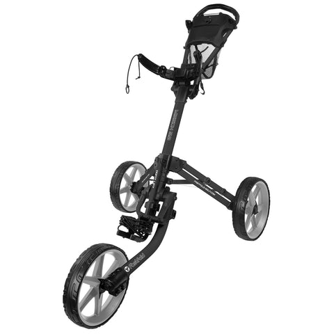 A black golf push cart stands upright with three wheels featuring a foot brake and a handlebar for steering in an outdoor setting, typically used for transporting golf bags on a course.