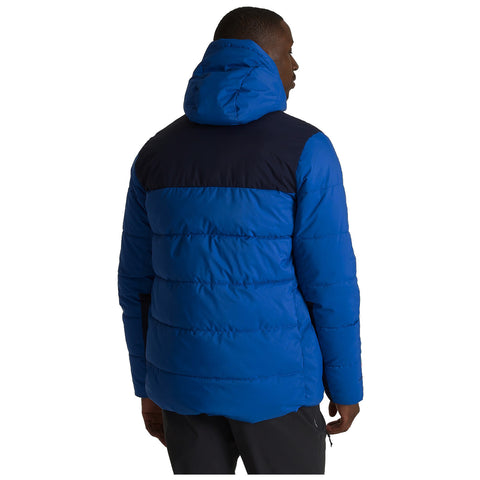 A blue puffer jacket with a black upper section is worn by a person viewed from the back. The individual stands in a neutral setting, suggesting casual wearability.