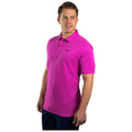 A man is standing and smiling while wearing a bright pink polo shirt. He is posed in a neutral setting, presenting a casual and confident appearance.