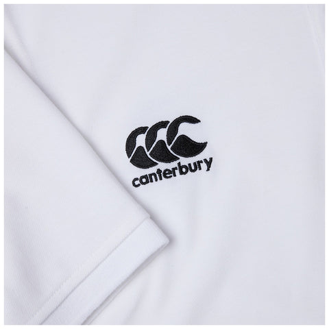 A white fabric shirt displays a black embroidered logo featuring three overlapping shapes and the word canterbury below it resting on a smooth surface.