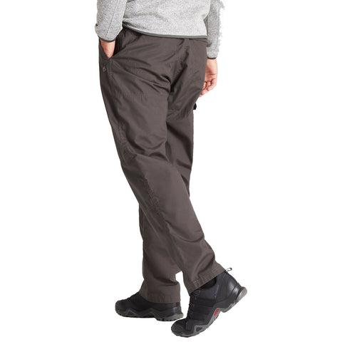 A person wearing dark pants and black footwear is standing with one foot slightly forward while casually resting one hand in their pocket in a neutral environment.