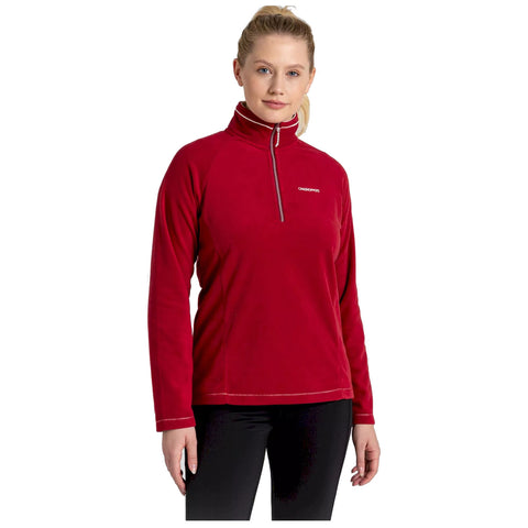 A woman is wearing a red fleece pullover with a half zipper and a logo on the chest while standing in a neutral background showcasing casual athletic wear.