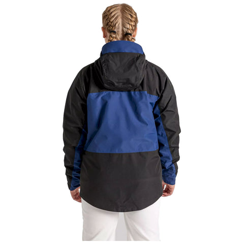 A person wearing a two-tone jacket with a blue upper section and black lower section stands with their back to the viewer in a neutral setting.