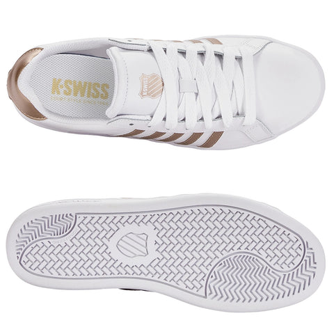 A white athletic shoe features three beige stripes on the side laces and a glossy beige accent on the heel placed against a plain background. The sole has a textured pattern.