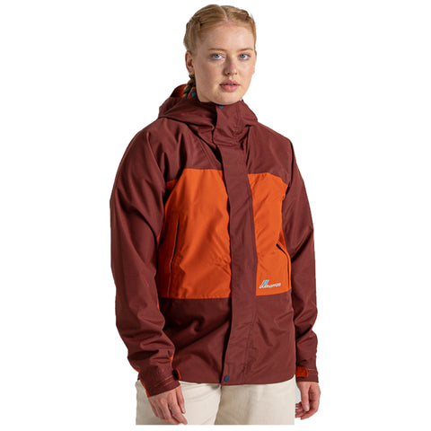 A person stands wearing a two-tone rain jacket featuring maroon and orange colors with a hood while looking directly at the viewer in a neutral setting.