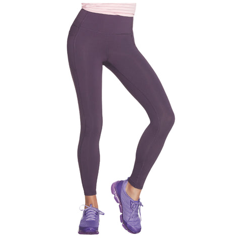 A person is standing with one leg forward wearing dark purple leggings and purple athletic shoes in a neutral setting typically associated with fitness or casual wear.