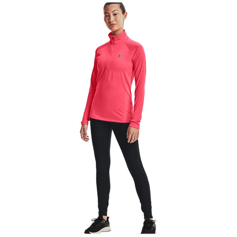 A woman stands confidently in a bright pink long-sleeve athletic top and black leggings, wearing black athletic shoes, in a neutral background that emphasizes her activewear.