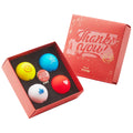 A red box holds five colorful golf balls with various designs and messages like "Thank you" and smiley faces set against a black foam background.