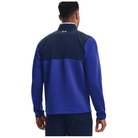 A person stands with their back facing the viewer wearing a blue and navy jacket with a high collar in a neutral background suggesting a focus on athletic apparel.